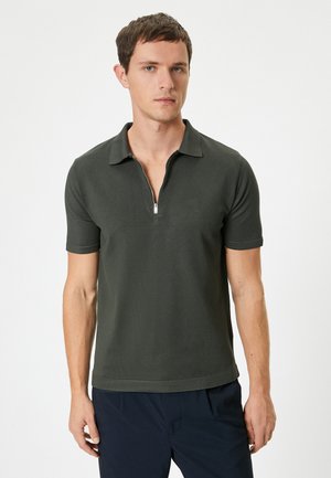 Kortærmet polo shirt i mørkegrøn med lynlåslukning ved kraven, tekstureret stof og en tætsiddende pasform. Pyntet med rene linjer og diskret syning.
