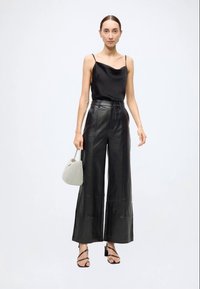 Schwarzes Satin-Camisole kombiniert mit schwarzen, weit geschnittenen Lederhosen. Eine graue, strukturierte Handtasche und schwarze Sandaletten mit Riemchen vervollständigen den Look.