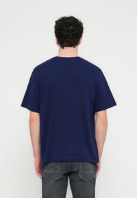 T-shirt a maniche corte di colore blu navy con scollo rotondo. Realizzata in morbido cotone, presenta una vestibilità rilassata e orli cuciti.