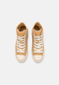 Nike sneakers de cano alto em couro bege claro com atacadores brancos e sola de borracha caramelo. Apresentam ilhós metálicos e um bico reforçado.