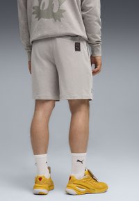Gray sweatshirt and shorts made of soft fabric. Yellow shoes with a textured design, white socks with black logo. Back view of the outfit.