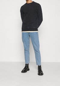 Černá vybledlá mikina s ribovanými manžetami, nošena přes světle barevné tričko, kombinována se světle modrými džíny se straight-leg a černými šněrovacími botami.