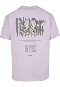 Lilla bomulds T-shirt med grå fugle med udstrakte vinger, teksten "FUGL AF FRED" og "Frihed" i stiliseret skrift nedenunder.