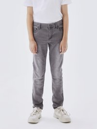 Jeans de mezclilla gris con un corte slim, que cuentan con un clásico diseño de cinco bolsillos, un ligero efecto de desgaste y cierre de botón. Llevados con zapatillas deportivas blancas.