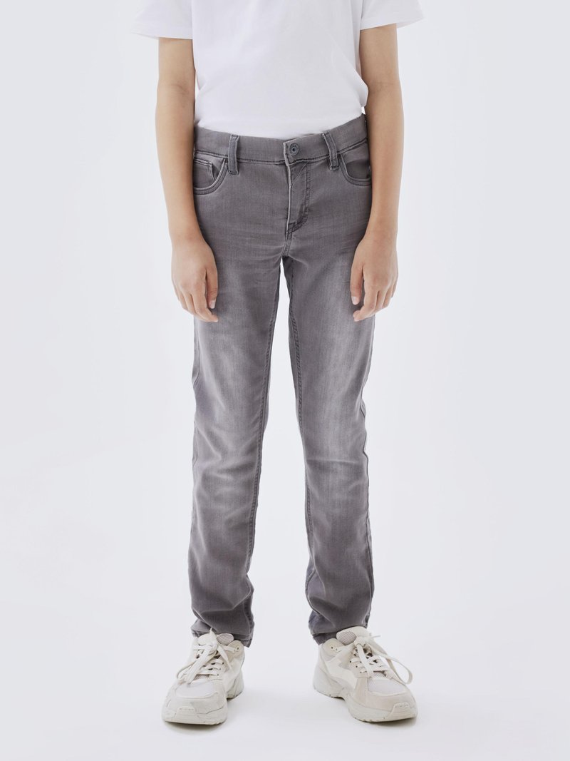 Jeans de mezclilla gris con un corte slim, que cuentan con un clásico diseño de cinco bolsillos, un ligero efecto de desgaste y cierre de botón. Llevados con zapatillas deportivas blancas.
