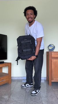 Mochila preta com alças ajustáveis, múltiplos compartimentos e detalhes em cordão elástico. Tecido suave e formato retangular.