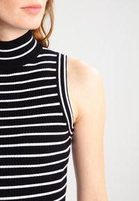 Haut sans manches à rayures noires et blanches avec un col montant, présentant une texture côtelée et une coupe ajustée.