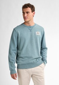 Felpa azzurra chiara in misto cotone, con colletto rotondo, polsini a coste e una patch sul petto con un'opera d'arte colorata.