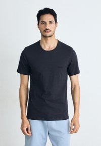 T-shirt noir à col rond en tissu léger et doux avec des manches courtes. Présente un logo discret sur la poitrine gauche et une coupe décontractée.
