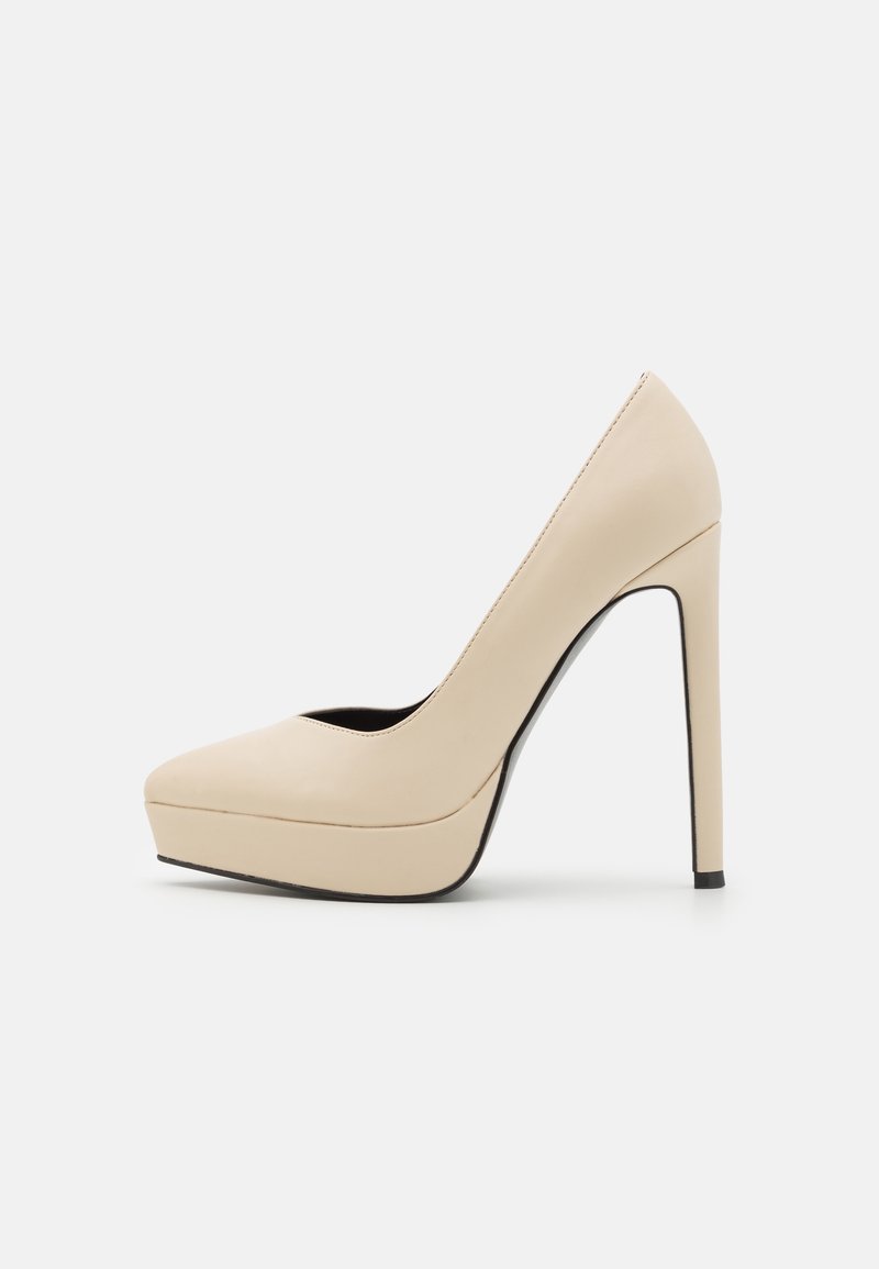 Escarpin beige à plateforme avec bout pointu et talon aiguilles fin sur fond blanc.