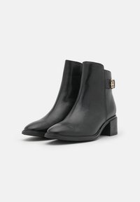 Bottes noires en cuir jusqu'à la cheville avec un bout pointu, un design minimaliste et un petit talon carré. Présente une sangle accentuée en doré.