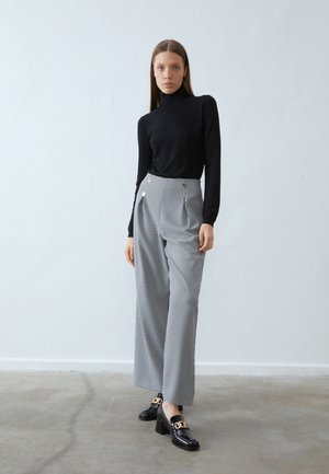 Black fitted turtleneck, wide-legged houndstooth trousers with front pleats and decorative gold buttons, paired with black block-heeled loafers.