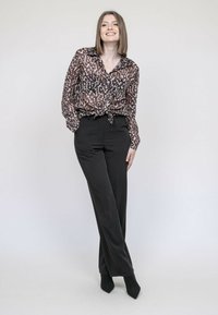 Chemise en imprimé léopard marron transparent nouée à la taille, associée à un pantalon noir taille haute et des escarpins noirs à bout pointu. Texture lisse et coupe décontractée.