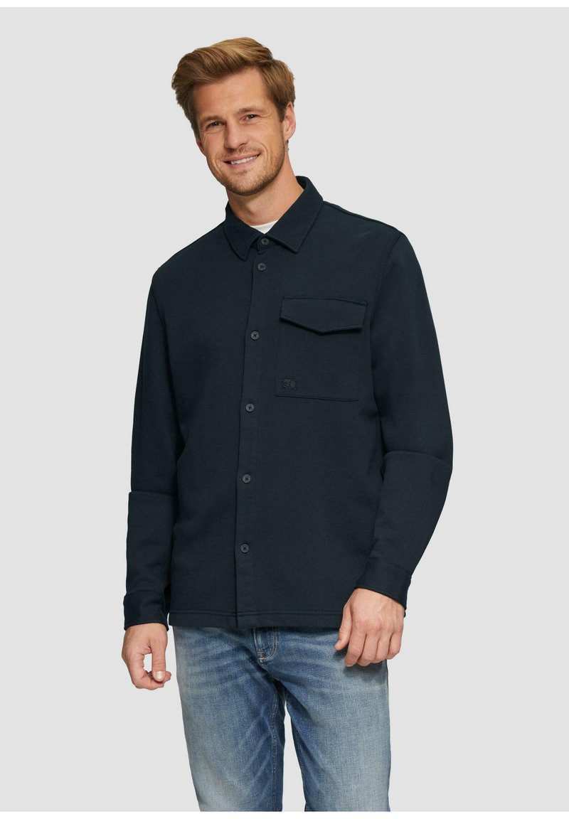 Marineblauwe button-up shirt met een subtiele textuur, voorzien van een enkele borstzak en een klassieke kraag, gecombineerd met lichtblauwe denim jeans.