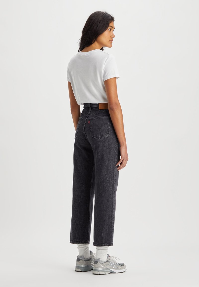 Jean noir taille haute avec un tissu texturé, t-shirt blanc court et baskets grises. Conçu avec une coupe droite et des poches arrière.