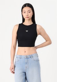 Svart ribbestrikket crop topp med rund halslinning, med en liten hjerte-logo i midten. Kombinert med lyseblå høyhyttejeans.