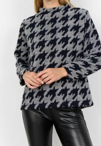 Grijze trui met zwart houndstoothpatroon, ronde hals, lange mouwen en een zachte textuur; gecombineerd met zwarte leren broek.