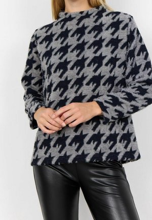 Pull gris avec un motif pied-de-poule noir, encolure ras du cou, manches longues et texture douce ; associé à un pantalon en cuir noir.