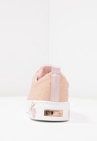 Zapatilla de glitter rosa con textura suave, que cuenta con una lengüeta de satén en el talón, un estampado floral en la suela y un acento de logo dorado.