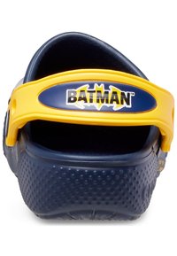 Chaussure marine à enfiler avec une semelle en caoutchouc texturé, une sangle ajustable jaune avec un logo "BATMAN", un dos arrondi et un design ouvert.