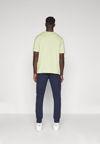 Lichtgroene t-shirt met korte mouwen gecombineerd met marineblauwe broek, met een relaxte pasvorm en minimalistisch ontwerp. Witte sneakers maken de look compleet.