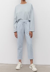 Svetle modrá mikina a odpovídající tepláky z měkkého materiálu. Mikina má dlouhé rukávy a zkrácený střih; tepláky mají elastický pas se šňůrkou.