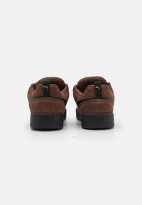 Brown suede sneakers with a black rubber sole, featuring a black stripe and logo at the heel, and a padded collar for comfort.