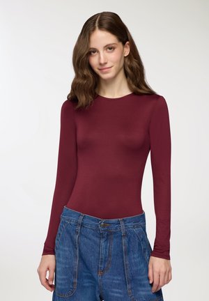 Body a maniche lunghe borgogna in tessuto elasticizzato, abbinato a pantaloni shorts in denim blu a vita alta con cuciture in vista e chiusura con bottone.