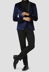 Námořnický sametový blazer s černým šálovým klopem, kombinovaný s černými kalhotami a lesklými černými botami, s přizpůsobeným střihem a hladkou texturou.
