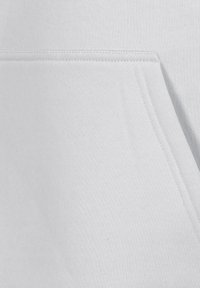 Hellgrauer Sweatshirtstoff mit einer Kängurutasche, glatter Textur und Nahtdetails im Bereich der Tasche.