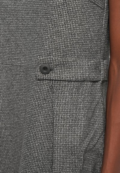 Grau kariertes Gewebe mit einer strukturierten Oberfläche, versehen mit einem schwarzen Knopf und einem seitlichen Taschendetail.