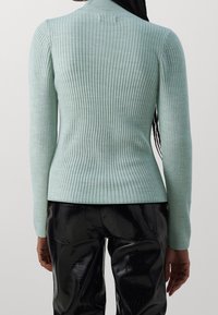 Mintgrüner, gerippter Pullover mit hohem Kragen und figurbetontem Schnitt, kombiniert mit glänzenden schwarzen Kunstlederhosen.