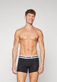 Black boxer briefs with a white waistband featuring a black double stripe and "PUMA" logo. Smooth fabric with a fitted design.