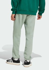 Ljusgröna sweatpants med avslappnad passform, med elastiska muddarna. Tillsammans med svarta och vita Adidas-skor och en grön sweatshirt.