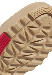 Sulkant med beige gummi som har en texturerad yta och triangulära mönster, accentuerad med ett rött rand.