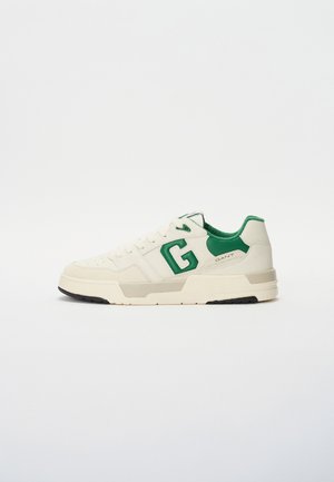 White sneaker with green accents, featuring smooth leather and suede, round toe, flat sole, and prominent 'G' logo on the side.