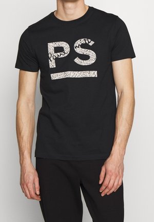 Mann trägt schwarzes kurzärmeliges T-Shirt mit großen weißen, rissigen Buchstaben "PS" und einer horizontalen Linie unter den Buchstaben.