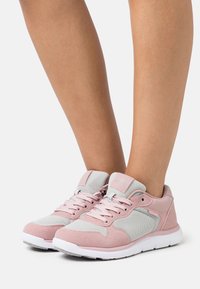 Rosa og grå atletiske sko med en strukturert semsket overflate, mesh-paneler og kontrasterende gummisåler. Snøringene er rosa; logoen er på tungen.