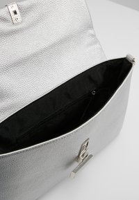 Silver textured handbag with a flap closure and metal hardware. Interior is black fabric featuring one zippered pocket.