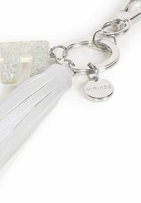 Portachiavi in acrilico trasparente con glitter, hardware metallico argentato, una frangetta bianca con texture e un'etichetta circolare incisa con la scritta "MIRIADA."