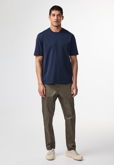 Marineblaues Baumwoll-T-Shirt mit Rundhalsausschnitt, kombiniert mit olivgrünen Hosen. Leichte Textur, gerade Passform und schlichtes Design ohne sichtbare Muster.