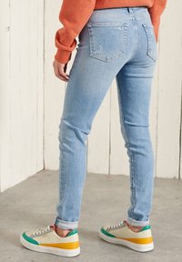 Ljusblå skinny jeans med slitna detaljer, ett par beigefärgade och färgglada sneakers. Lätt textur, medelhög midja och uppvikta ben.