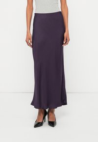 Saia longa e fluida de cor roxa, feita de tecido suave, com um ligeiro brilho e bainha evasê. Combinada com sapatos pretos de salto alto.