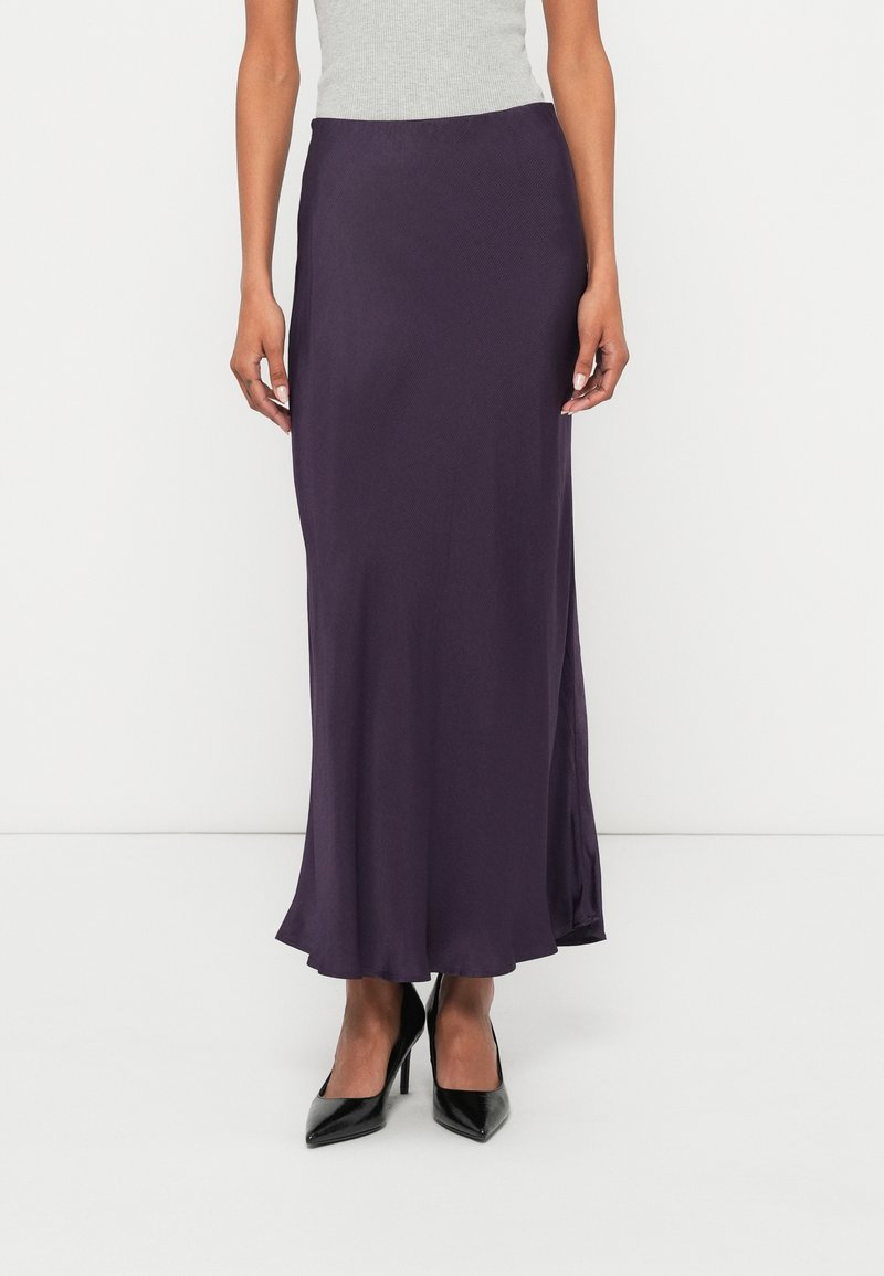 Saia longa e fluida de cor roxa, feita de tecido suave, com um ligeiro brilho e bainha evasê. Combinada com sapatos pretos de salto alto.