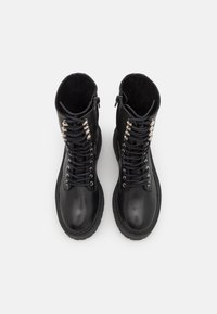 Bottes de combat en cuir noir avec bouts ronds, lacets et œillets métalliques. Fermeture éclair sur un côté, intérieurs texturés, semelles en caoutchouc robustes.