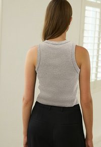 Débardeur gris côtelé avec un col rond, sans manches et une silhouette ajustée, associé à un pantalon noir avec des poches arrière.