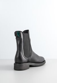 Schwarze Leder-Ankle-Boots mit elastischen Seitenpanelen, runder Zehenpartie und niedrigem, gestapeltem Absatz. Mit einem grünen Akzent auf der Rückseite.