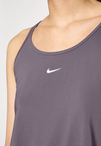 Lilla atletisk tanktop lavet af glat stof, med en rund udskæring og et lille hvidt Nike-logo på midten af brystet.