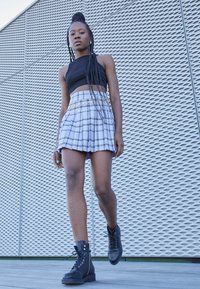 Top corto negro, mini falda de cuadros con herrajes dorados y botas de combate negras. Texturas suaves; patrón elegante con líneas alternas.