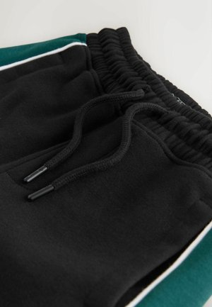 Sorte sweatpants med elastisk taljebånd og sorte snore, kontrasterende grønne sidepaneler og hvide detaljer.